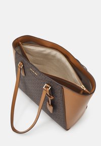 Michael Kors bruine schoudertas met logo-patroon, tanleren handvatten en een bovenste ritscompartiment met beige stoffen voering.