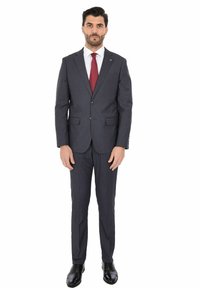 Completo grigio scuro con una vestibilità su misura, caratterizzato da revers a punta, chiusura a due bottoni e pantaloni con gamba dritta. Abbinato a una camicia bianca e una cravatta bordeaux.