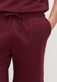 Maroon cotton joggers with an elastic waistband, drawstring detail, and side pockets; soft texture and relaxed fit.
