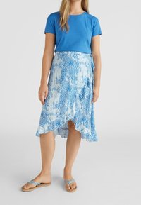 Camiseta de manga corta azul combinada con una falda pareo azul y blanca con estampado y dobladillo con volantes, complementada con sandalias azules.