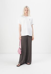 Hvit bomull t-skjorte, svart og hvit stripete vidbukser, rosa håndveske og svarte sandaler. Modellen står foran en ensfarget bakgrunn.