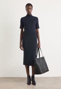 Navy fitted turtleneck, knee-length pencil skirt, and black leather tote bag. Model wearing black pointed ankle boots. Smooth textures.