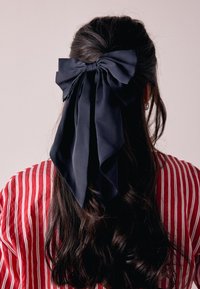 Marineblaues Satin-Haaraccessoire mit langer, fließender Schleife, kontrastierend zu einem rot gestreiften Hemd. Glatte Textur und weicher Fall.