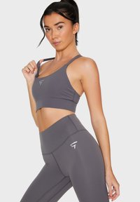 Reggiseno sportivo grigio e leggings a vita alta coordinati realizzati in tessuto liscio e elastico. Presenta un dettaglio del logo sulla gamba sinistra e spalline regolabili.