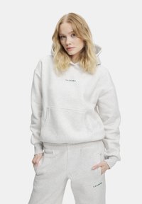 Ljusgrå hoodie gjord av mjukt tyg med en kenguruficka. Har en grön logotryck. Matchas med ljusgrå mjukisbyxor.