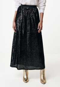 Schwarze Pailletten-Maxiröcke mit einem gerafften Taillenbund, der eine glänzende Textur und ein flatterndes Design aufweist. Getragen mit metallisch goldenen Ankle Boots.