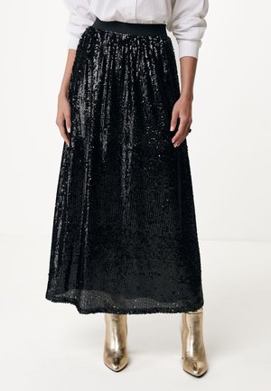 Jupe maxi noire en sequins avec taille froncée, présentant une texture brillante et un design fluide. Associée à des bottines dorées métalliques.