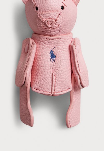 Roze leren berenfiguur met een gestructureerd oppervlak, zichtbare stiksels en een blauw geborduurd polologo op de borst. Armen zijn beweegbaar.