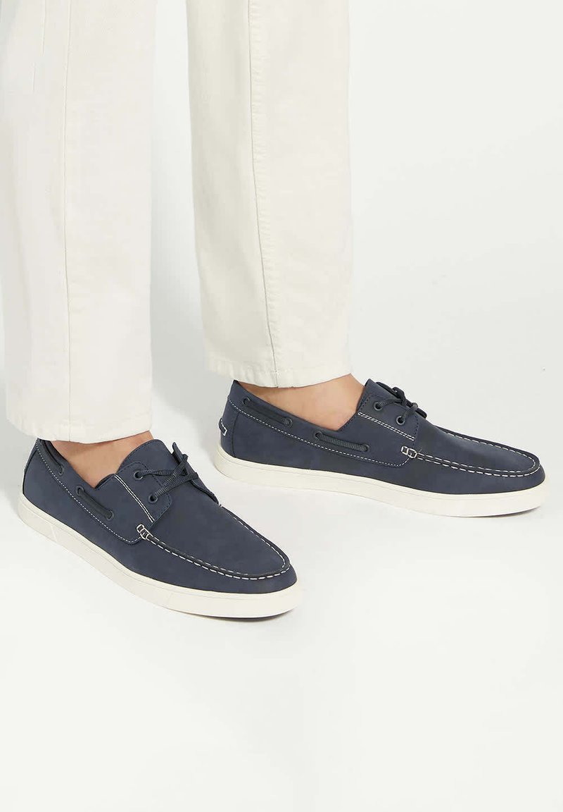 Navy blue casual shoes made of soft material, featuring white stitching, lace-up design, and a white rubber sole.