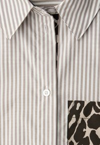 Chemise à rayures beige clair et blanc avec un col classique, fermeture boutonnée, et un accent de poche à imprimé léopard. Texture de tissu lisse.