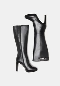 Black leather knee-high boots with a pointed toe, stiletto heel, and side zipper. Smooth texture with a subtle sheen and hardware accents.