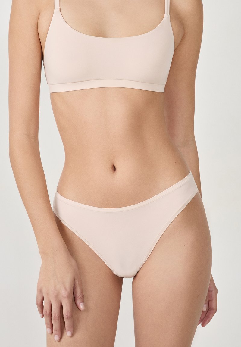 Ensemble de lingerie deux pièces nude comprenant un soutien-gorge sans couture et extensible avec des bretelles fines et un bas de bikini assorti dans une finition mate lisse.