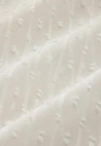 Vit texturerad tyg med upphöjda prickar och tunna vertikala ränder som skapar ett subtilt mönster. Mjukt, lättmaterial med en ömtålig utseende.