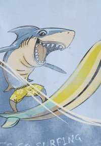 Cartoonhaai met een brede glimlach rijdt op een gele surfplank, terwijl hij bloemenzwemshorts draagt, tegen een lichtblauwe achtergrond.