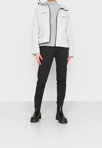 Light grey jacket with a hood, two front pockets, and a zipper. Worn over a textured grey sweater and black slim-fit pants, with black ankle boots.