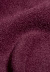 Bordowy materiał o miękkiej, teksturowanej powierzchni, z gładkimi krzywiznami i subtelnym połyskiem, idealny do tapicerki lub zastosowań modowych.