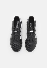 Svarta fotbollsskor med en texturerad ovandel, som har vita ränder och snören. Designen inkluderar ett kviltat mönster och en gummisula.