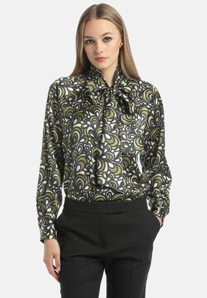 Blusa bianca e nera con un motivo paisley verde, caratterizzata da maniche lunghe, un collo a fiocco e una texture satinata liscia. Indossata con pantaloni neri.