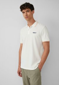 Weißes Poloshirt mit orangefarbenem und weißem gestreiften Kragen, gesticktem Logo auf der Brust, kurzen Ärmeln und glattem, strukturiertem Stoff.