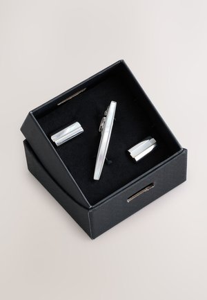 Black gift box containing a silver tie clip and matching cufflinks with smooth, polished rectangular designs on black fabric insert.