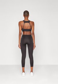 Svart atletisk crop top med utskåret ryggdetalj, kombinert med høyt liv svarte leggings. Glatt, stretchy stoff og ankellang design.