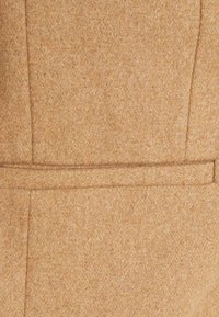 Tessuto in lana strutturato di un caldo beige, con un taglio dritto e un sottile dettaglio di cucitura al centro per un design strutturato.