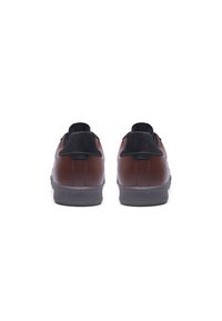 Brown leather sneakers featuring a black suede accent at the heel, flat grey rubber sole, and minimalistic design with contrasting stitching.