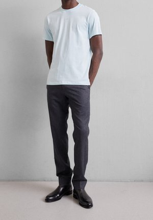 Helles blaues Baumwoll-T-Shirt mit Rundhalsausschnitt, kombiniert mit dunkelgrauen, maßgeschneiderten Hosen und schwarzen Ankle Boots. Einfaches Design, keine auffälligen Muster.