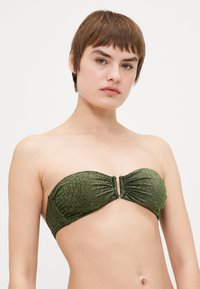 Žalias blizgučių bandeau tipo bikinio viršus su susiraukšlėjusiais audiniais ir dekoratyviu priekinio sagties užsegimu. Lygi tekstūra su blizgančiu paviršiumi.