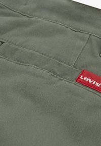 Λαδί ύφασμα με απαλή υφή, με μηχανική ραφή και ετικέτα Levi's σε κόκκινο χρώμα στο πλάι. Δύο τσέπες είναι ορατές.