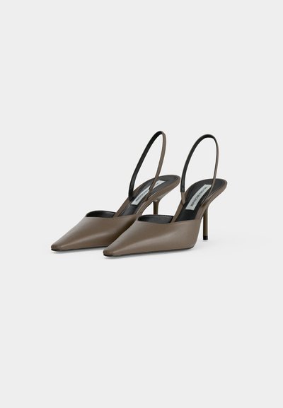 Γόβες slingback ταουπ με μυτερή μύτη, λεπτές λουρίδες και λεπτά ψηλά τακούνια σε απλό ανοιχτό γκρι φόντο.