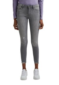 Jeans ajustados grises con detalles desgastados, con cintura alta, dobladillo deshilachado y diseño de cinco bolsillos. Combinados con zapatillas blancas.