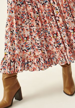 Falda midi con estampado floral y dobladillo con volantes combinada con botas de cuero color marrón claro de tacón alto sobre un fondo liso.