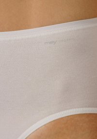 Světle béžové vysoké kalhotky vyrobené z měkkého, pružného materiálu s hladkými okraji a tkaným pasem. Minimální branding blízko pasu.