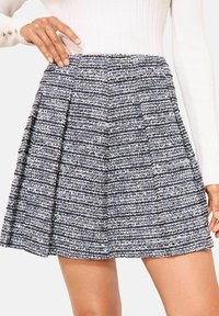 Tumši zili baltas teksturētas mini svārki ar krokojumu, izgatavoti no austas auduma. Raksturo piemērots viduklis un viegla tekstūra.