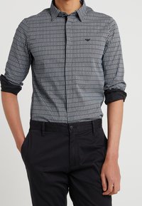 Långärmad skjorta med knappar i svart och vitt med ett rutmönster. Har en klassisk krage och uppkavlade ärmar, tillsammans med svarta byxor.