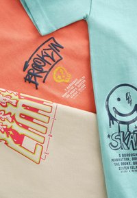 Tre kortärmade T-shirts i livliga färger: teal, korall och kräm. Var och en har djärva grafiska tryck och text med olika mönster.