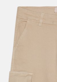 Pantaloni in cotone beige con una texture liscia, passanti per cintura, tasche laterali e dettagli di cucitura intricati.