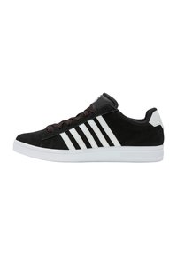 Zapatillas de ante negro con diseño de tres rayas blancas, cordones marrones y suela de goma blanca. Silueta de perfil bajo con cuello acolchado.