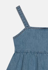 Sukienka dżinsowa z cienkimi ramiączkami, w jasnoniebieskim kolorze, z marszczonym pasem. Materiał ma miękką teksturę, z widocznymi detalami przeszyć.