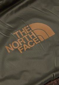 Grøn stofoverflade med "THE NORTH FACE" logo i brun, med et halvcirkeldesign. Materialet ser glat og tekstureret ud.