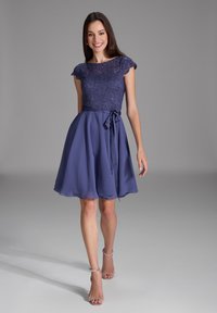 Robe violette avec un corsage en dentelle et des manches courtes, jupe fluide, et un ruban assorti à la taille. Texture lisse, design jusqu'aux genoux.