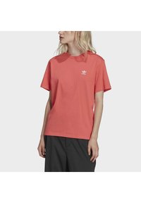 Korálové bavlněné tričko s krátkými rukávy a kulatým výstřihem. Obsahuje malé bílé logo Adidas na horní části levé hrudi.