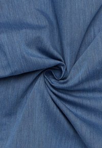 Tessuto denim di un blu medio, che mostra una consistenza liscia e sottili variazioni di colore, torcigliato per evidenziare la sua flessibilità.