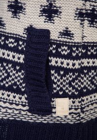 Stickad tröja med marinblå och krämfärgad Fair Isle-mönster, texturerat garn, rund hals och en liten varumärkesetikett på sidan.
