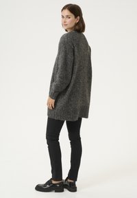 Pulover din tricot de culoare gri închis, supradimensionat, cu margine ribbed, purtat peste blugi negri conici și pantofi negri lucioși, având o siluetă lejeră.