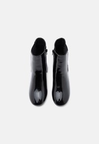 Botas de tobillo negras de charol con una textura suave, punta redonda, detalle de cremallera lateral y un acabado brillante y elegante.