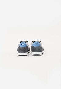 Šedé semišové a syntetické tenisky s modrými akcenty, bílou podešví a zakřiveným designem. Mají zaoblený podpatek a texturovaný povrch.
