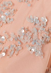 Tecido de malha pêssego ornamentado com lantejoulas iridescentes dispersas, apresentando uma textura delicada e um brilho subtil em toda a sua extensão.