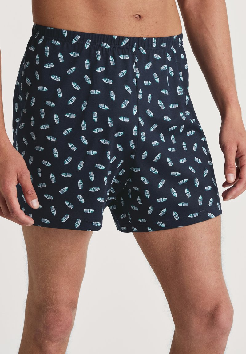 Marineblauwe katoenen boxers met een herhalend patroon van lichtblauwe en witte zeilboten, voorzien van een elastische tailleband en een losse pasvorm.